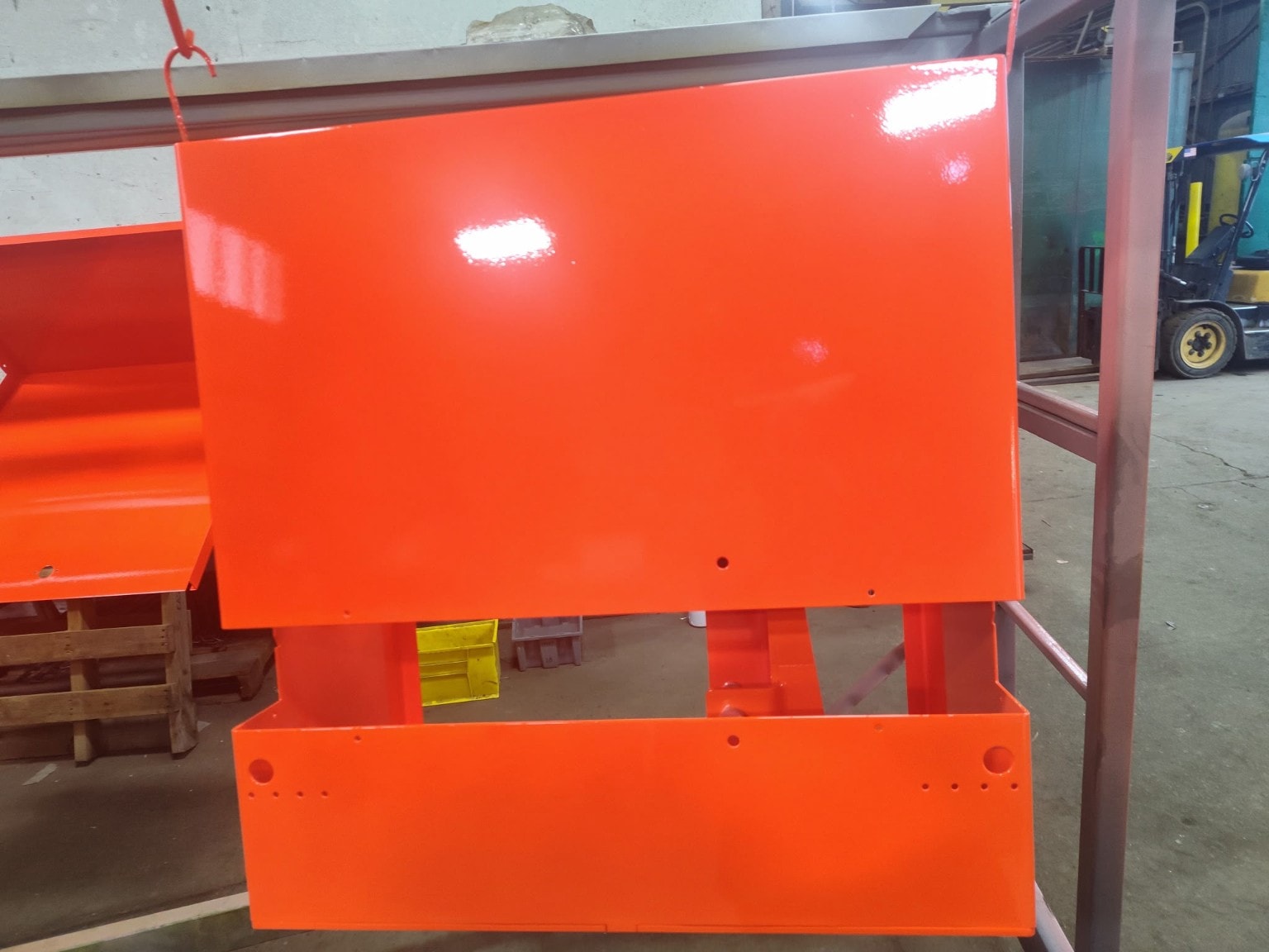Gloss orange powder-coated metal panels hanging on a rack inside the Apex facility