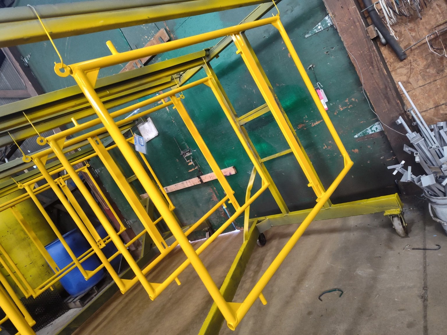 Yellow powder-coated metal tube frames hanging inside the Apex Powder Coating facility